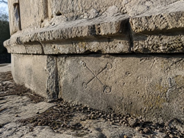 Carved mark on the foundation course of the chapel of St. John the Baptist, Křemešník. Two crossed lines with small circles at each end, approximately 8–9 cm across. Photographed at low angle in morning light; the mark is illegible in direct or flat illumination. kremesnik.jpg